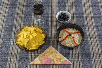 Bowl of tuna salad, tortilla chips, olives and glass of red wine.