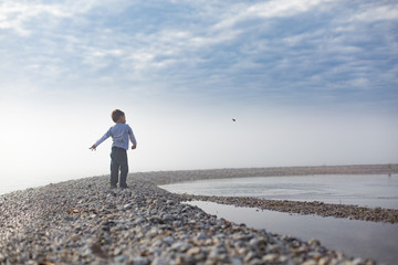 Boy standing on pebbled beach throwing pebbles