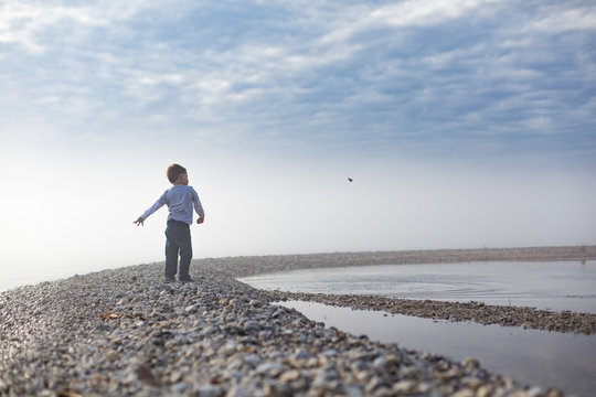 Boy standing on pebbled beach throwing pebbles