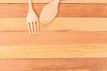 Top view of wooden fork and spoon on light wooden background.