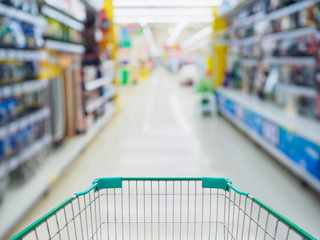 Supermarket aisle with empty green shopping cart blurred background