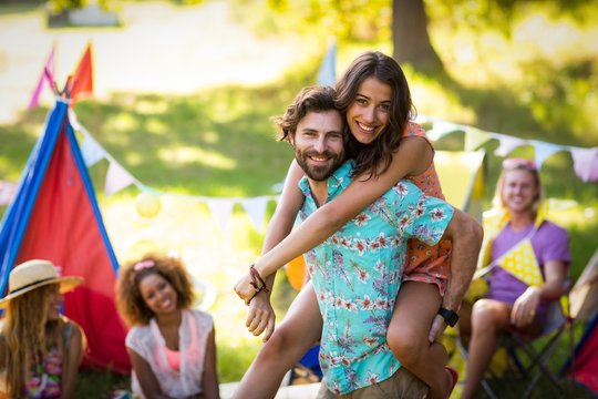 Man carrying woman on piggyback at campsite - Powered by Adobe