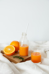 Orange fresh for breakfast in a glass and in a bottle with a straw. On the wooden board lies an orange and a magazine. Healthy breakfast in bed, daylight, vertical shot.