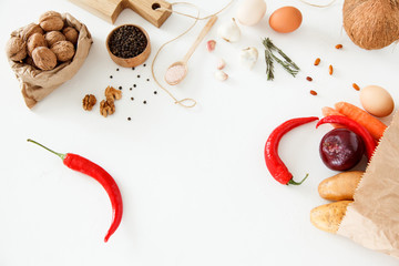 Vegetables, nuts, beans, potatoes, red peppers, chicken eggs, other food and kitchen appliances lie on a white background. Space for text, daylight, horizontal image.