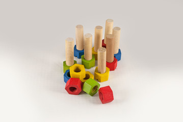 Colorful wooden toy nuts and bolts arranged and isolated on grey gradient background, studio shot