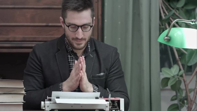 Young author in glasses rubbing his hands and starting typing on a red vintage typewriter