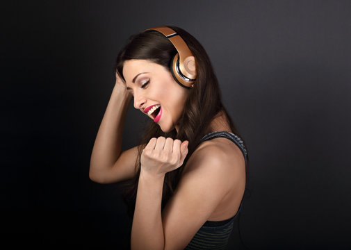 Beautiful happy dancing young woman listening the music in wireless headphone on dark grey background