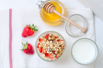 Top view healthy breakfast of homemade granola cereal with milk, strawberry, nuts and fruit, honey with drizzlier on white background. Morning food, Diet, Detox, Clean Eating, Vegetarian concept.