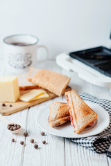 Hearty and traditional breakfast, sandwiches with rye toast, sausage, cheese, spices and black tea on a light wooden background