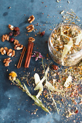 Cinnamon sticks, nuts and a herb collection scattered on a blue table, a glass jar with tea, lime, mint, lemon balm, chamomile. Daylight, vertical image.