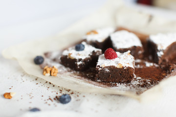 Table setting, chocolate dessert brownie cake with berries on parchment paper on a table covered with a linen tablecloth. Horizontal shot, daylight.