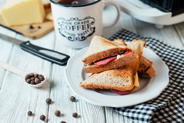 Hearty and traditional breakfast, sandwiches with rye toast, sausage, cheese, spices and black tea on a light wooden background