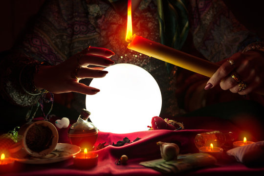 Woman fortune teller holding candle above crystal ball