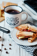 Hearty and traditional breakfast, sandwiches with rye toast, sausage, cheese, spices and black tea on a light wooden background