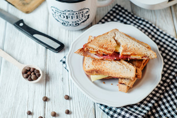 Hearty and traditional breakfast, sandwiches with rye toast, sausage, cheese, spices and black tea on a light wooden background