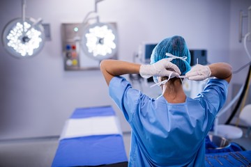 Female nurse tying surgical mask in operation theater - obrazy, fototapety, plakaty