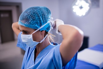 Female nurse tying surgical mask in operation theater - Powered by Adobe