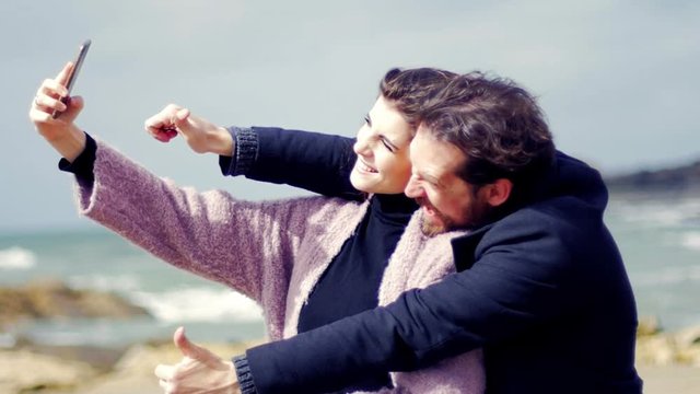 Very happy couple in love taking selfie on the beach in winter slow motion medium shot