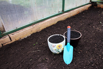 Ceramic flowerpots filled with the fresh soil for planting and a garden trowel in the polycarbonate greenhouse prepared for wintering