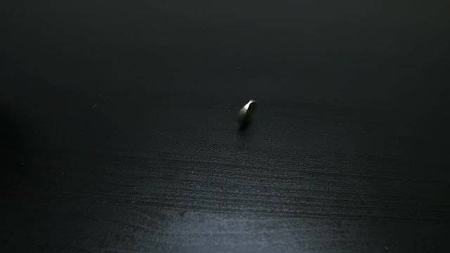 The coin is turned over. The coin rota tes close to the camera, slows and falls. Slow motion.