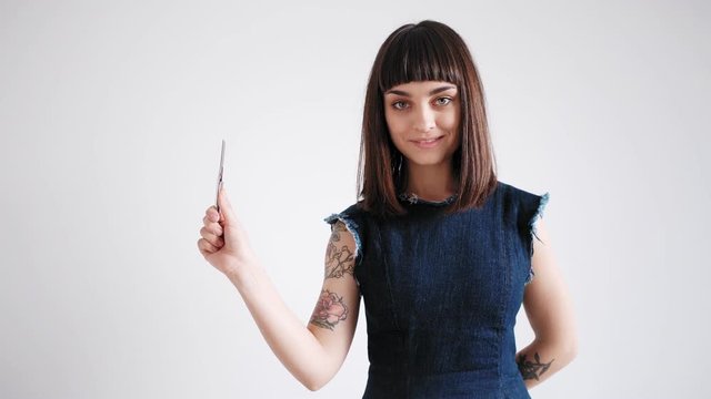 Brunette cute girl wearing a femenine dress brings up a sharp stationery knife, smiling and looking at camera prepared to open her newly arrived package