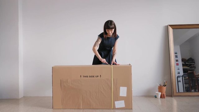 An attractive young female opens up a recently received impressive cardboard parcel with a cutting knife in excitement and awe