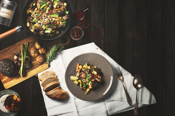 Overhead view of colorful roast vegetables, savory sauces and salt served with grilled t-bone steak...
