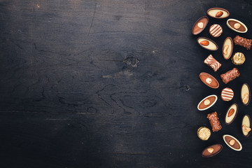 Assortment of chocolates with nuts. Black and milk chocolate. Wooden on the black surface. Top view.