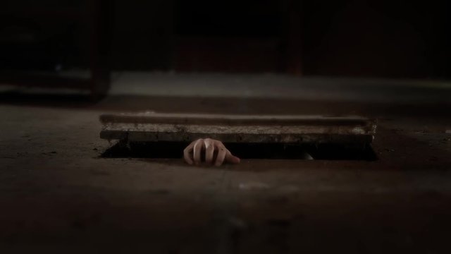 A creepy hand crawls out of a cellar trap door. 