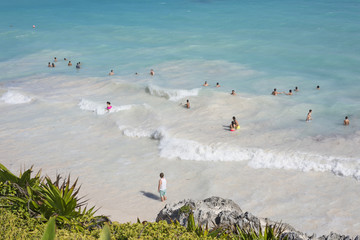 Top view of the Caribbean Sea under blue sky with swimmers on the beach in Tulum, Yucatan Peninsula, Mexico, green tropical plant palm trees foreground