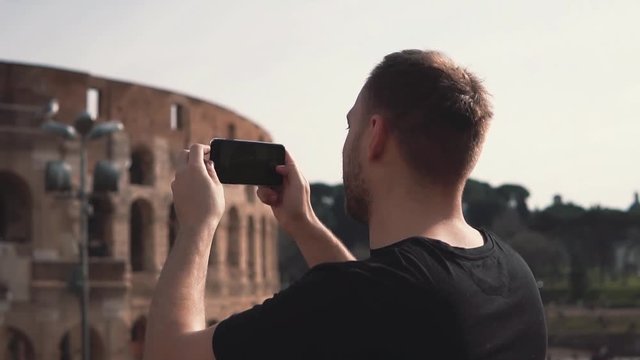 Handsome man tourist visiting Rome, Italy take photos of Colosseum. Landscape with tourists on background. Slow motion.