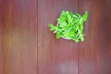 Raw arugula lettuce in a white plate on a wooden table