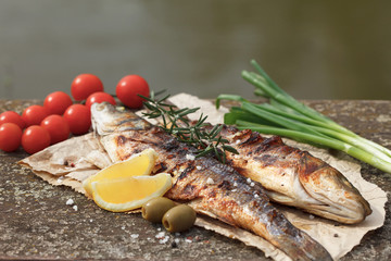 Grilled sea bass served on a paper with tomato and onion and decorated with rosemary and lemon