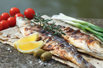 Grilled fish served on a paper with tomato,m onion and olives and decorated with rosemary and lemon