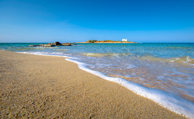 Typical summer image of an amazing pictorial view of a sandy beach with an old white church in a small island at the background, Malia, Crete, Greece.
