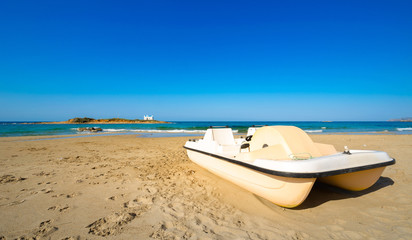 Typical summer image of an amazing pictorial view of a sandy beach with a boat on the beach and an old white church in a small island at the background, Malia, Crete, Greece.