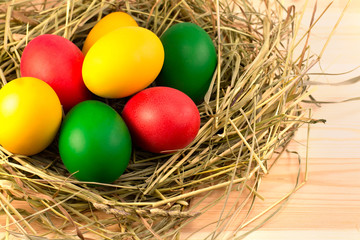 Fototapeta na wymiar Easter eggs, painted in green, red, yellow, lie in a nest of hay