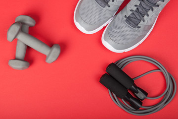 Sport shoes, dumbbells and skipping rope on red background. Top view. Fitness, sport and healthy...