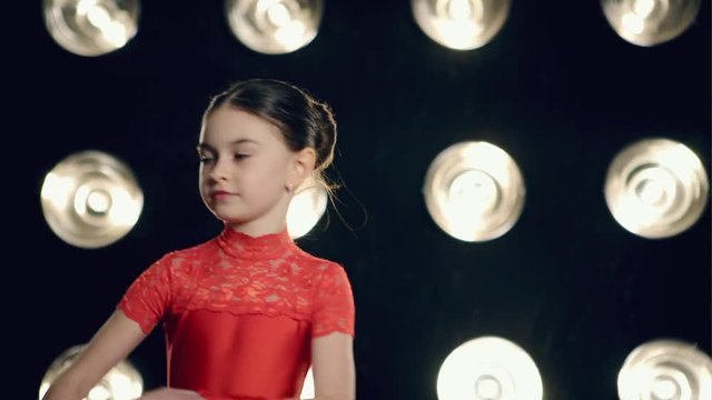 The young girl in red dress dancing cha-cha-cha on stage in bright light