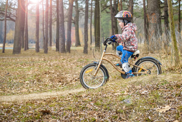 Fototapeta premium child on a bicycle in the forest in early morning. Boy cycling outdoors in helmet