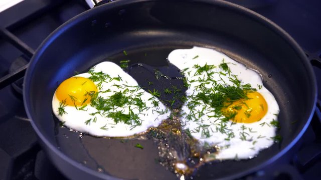 Fried eggs  sprinkled with parsley on a black frying pan closeup 