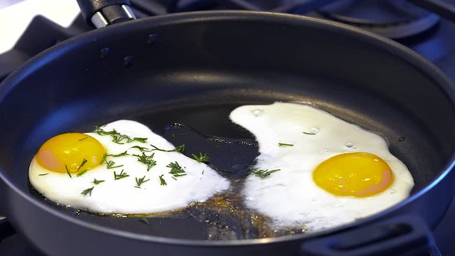 Fried egg  sprinkled with parsley on a black frying pan closeup slow motion