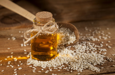 Fresh sesame oil in a glass bottle and seeds in a wooden spoon
