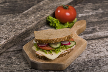 Healthy sandwich made with whole grain bread, lettuce, tomato, radish, cheese and roasted chicken slices.