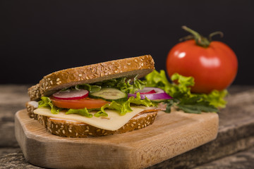 Healthy sandwich made with whole grain bread, lettuce, tomato, radish, cheese and roasted chicken slices.