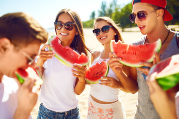 Group of friends having fun eating watermelon. on the beach. Excellent sunny weather. Beautiful figures. Super mood. Summer concept
