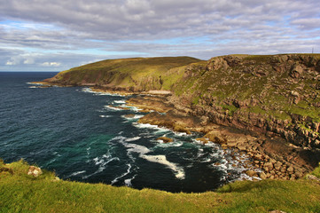 Naklejka premium Rocky coast with steep cliffs, waves, sky, clouds