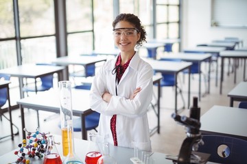Portrait of schoolgirl in lab coat standing with arms crossed in laboratory