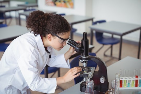 Attentive schoolgirl looking through microscope in laboratory