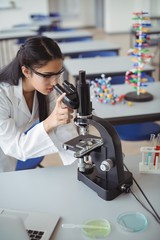 Attentive schoolgirl looking through microscope in laboratory